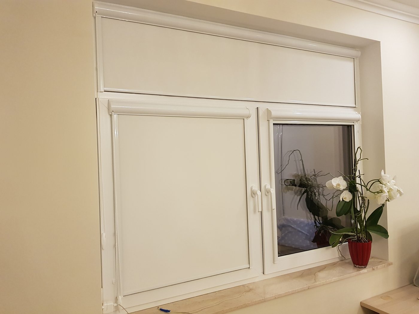 Baltas kasešu žalūzijas logā ar augšējo vērtni — kasete uz katras vērtnes Baltas kasešu žalūzijas logā ar augšējo vērtni — kasete uz katras vērtnes